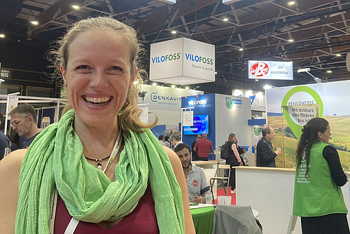 Ein Frau lacht strahlend, im Hintergrund eine Landwirtschaftsmesse.