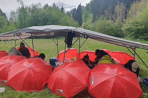Entre les auvents, de nombreux parapluies rouges sont déployés, sous lesquels des personnes travaillent. 