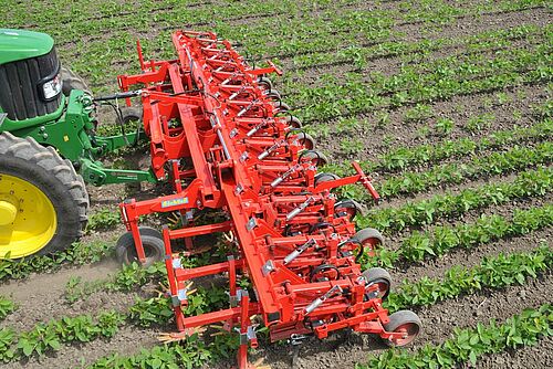 Sarcleuse rouge devant un tracteur dans un champ