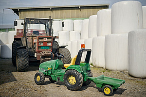Véritable tracteur et tracteur jouet devant des balles de silo empilées.