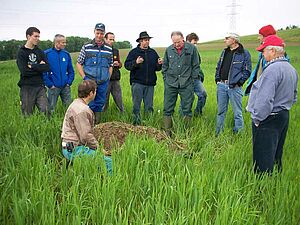 Conseiller agricole dans une petite fosse au milieu d'un champ de céréales, entouré d'agriculteurs qui écoutent les explications du conseiller