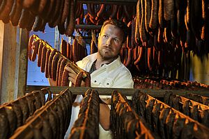 Un homme avec plusieurs barres pleines de saucisses dans une entreprise de production.