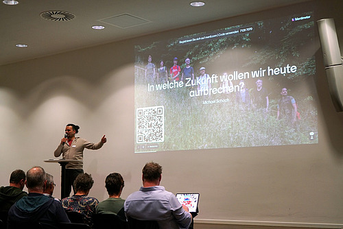 Ein Mann präsentiert vor einer Powerpoint-Präsentation.