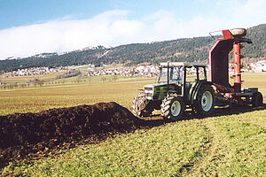 Un tracteur se trouve devant un endain de compost en plein champ avec une machine à retourner les endains