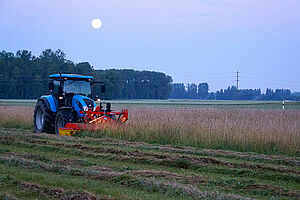 Taktor avec faucheuse frontale fauchant une prairie fleurie le soir