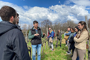 Un groupe de personnes écoute un orateur dans un vignoble.