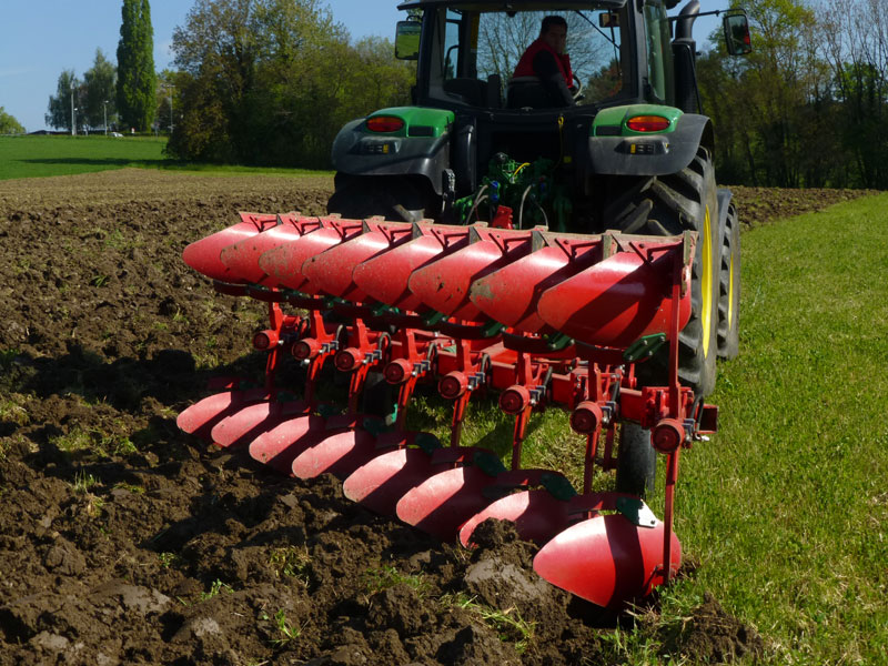 Charue rouge en plein ttravail dans une prairie.